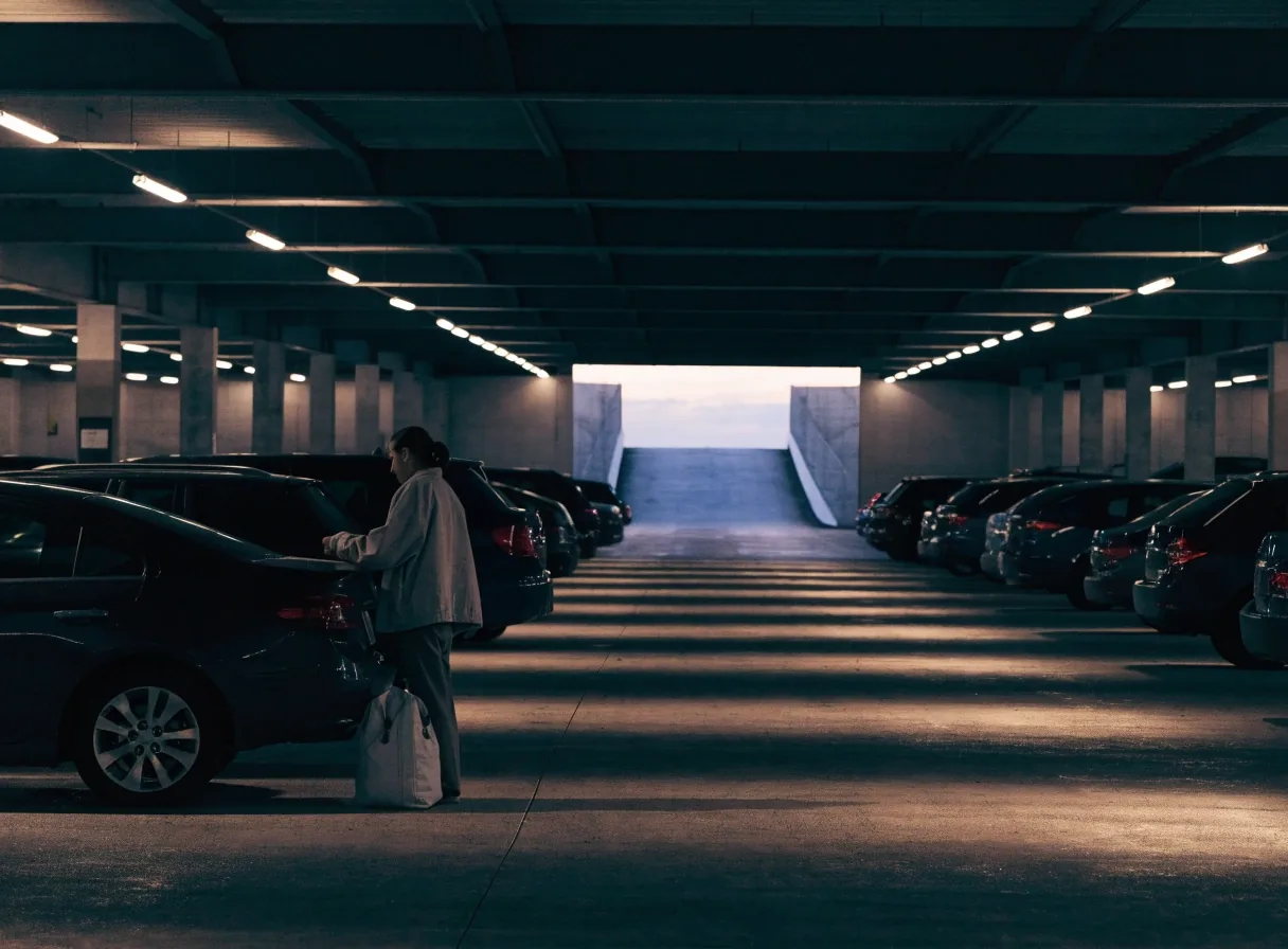 Traveller closing a car door on a covered airport car park level in the evening